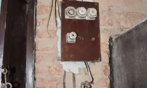 Stara instalacja elektryczna z ceramicznymi bezpiecznikami i widocznymi przewodami na ceglanej ścianie.