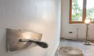 Gładź nakładana kielnią na ścianę. W tle okno i lampa budowlana.