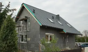 Dobudówka do starego domu w trakcie budowy. Szary, betonowy budynek z szarym dachem, oknami i rusztowaniami.