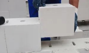 Ręce w rękawiczkach układają biały pustak silikatowy na budowie.
