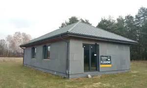 Gotowe domy pod klucz do 150 tys. zł. Nowoczesny, parterowy budynek z szarej cegły, z szarym dachem i dużymi oknami.