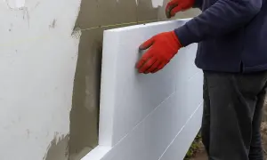Pracownik w czerwonych rękawicach montuje styropian na ścianie. Poznaj cenę ocieplenia za 1m2 robocizna.