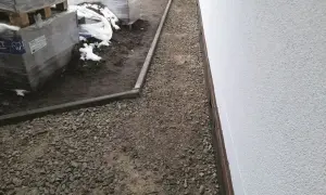 Wykonano opaskę wokół domu z żwiru, obok składowane są materiały budowlane.