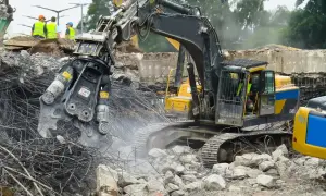 Maszyna budowlana z chwytakiem hydraulicznym prowadzi rozbiórkę betonowej konstrukcji, krusząc ją na drobne kawałki.