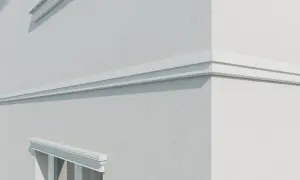 Biały, ozdobny gzyms biegnie wzdłuż chropowatej, jasnej ściany budynku, podkreślając jego architekturę.