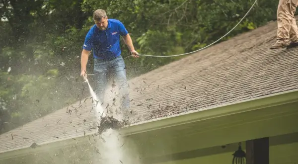 Mężczyzna myje dach myjką ciśnieniową, usuwając liście. Sprawdź, jaka jest mycie dachu cena i zadbaj o swój dom.