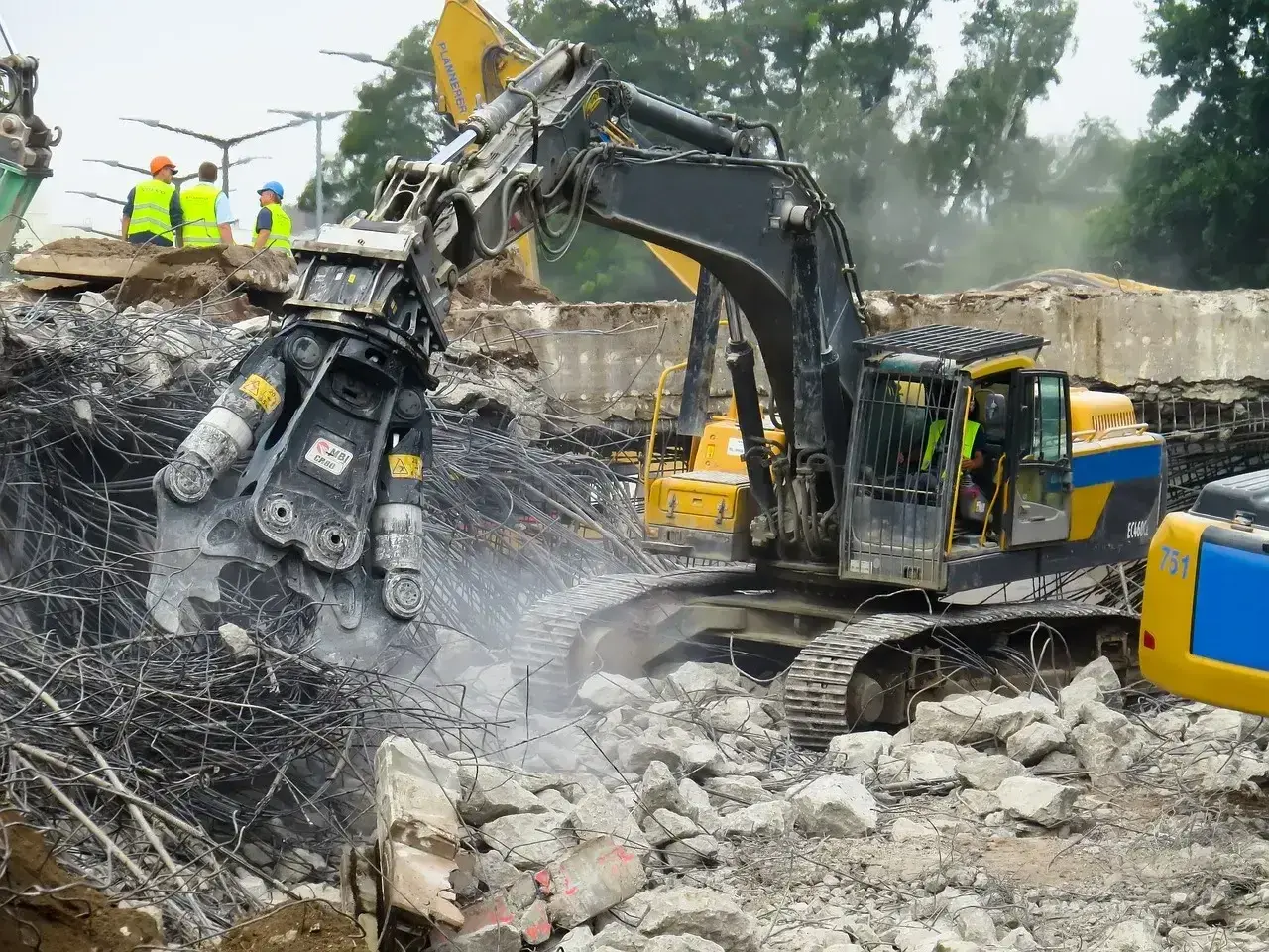 Maszyna budowlana z chwytakiem hydraulicznym prowadzi rozbiórkę betonowej konstrukcji, krusząc ją na drobne kawałki.