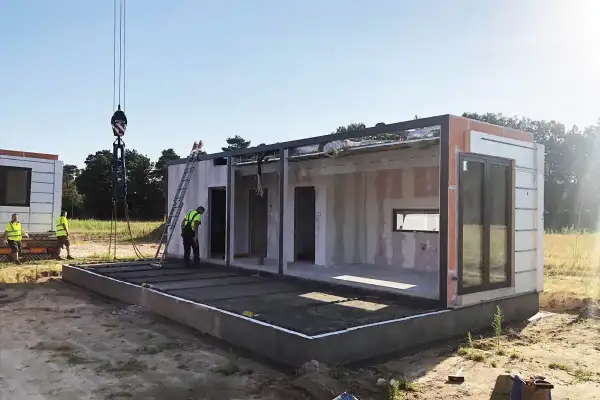 Budowa domu modułowego w toku. Dźwig podnosi element konstrukcji. Pozwolenie na budowę zostało uzyskane, prace postępują.