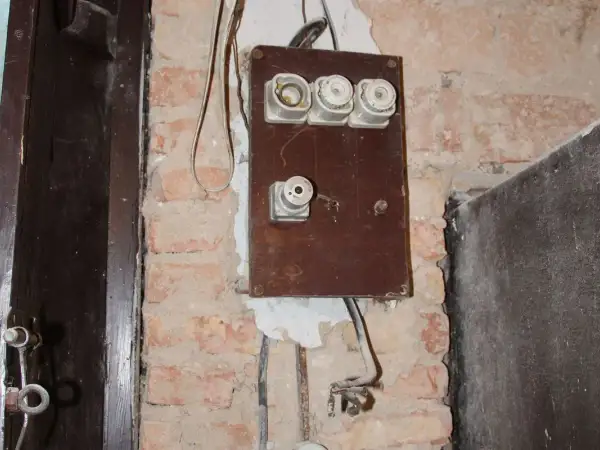 Stara instalacja elektryczna z ceramicznymi bezpiecznikami i widocznymi przewodami na ceglanej ścianie.