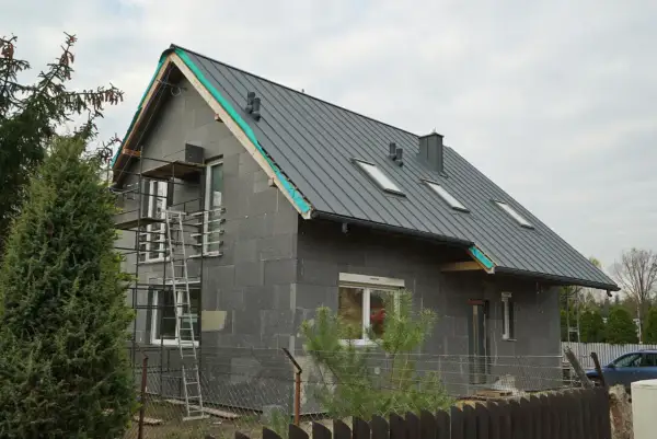 Dobudówka do starego domu w trakcie budowy. Szary, betonowy budynek z szarym dachem, oknami i rusztowaniami.