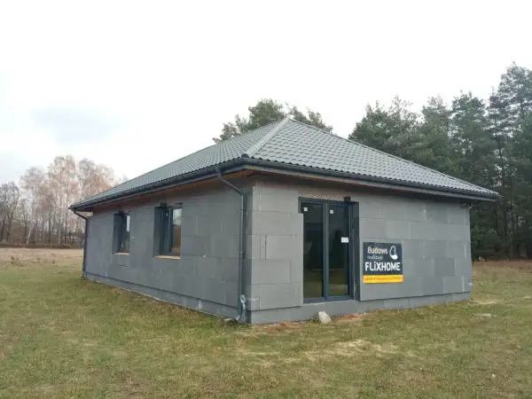 Gotowe domy pod klucz do 150 tys. zł. Nowoczesny, parterowy budynek z szarej cegły, z szarym dachem i dużymi oknami.