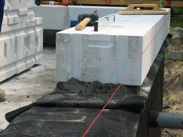 Budowa domu: układanie bloczków z betonu komórkowego, zastosowano izolację poziomą fundamentów, narzędzia budowlane.