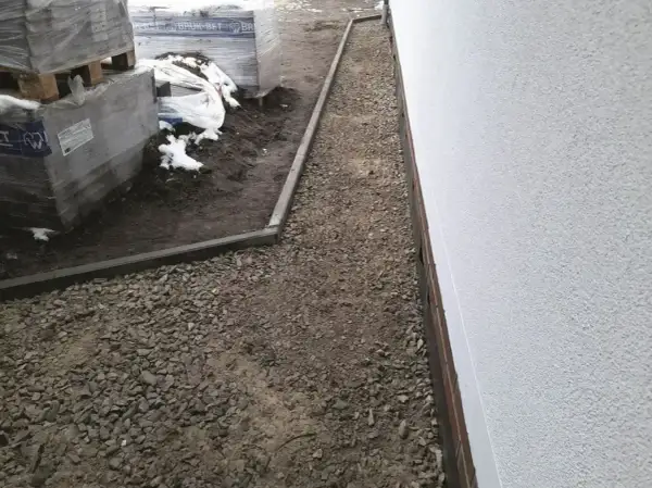 Wykonano opaskę wokół domu z żwiru, obok składowane są materiały budowlane.